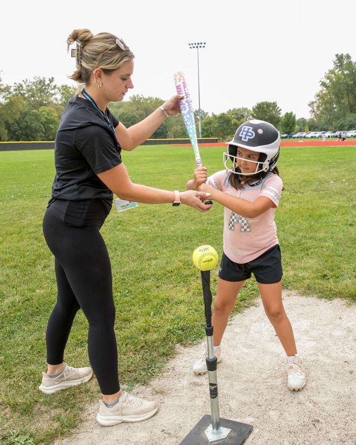 Taelor Schmitz coaches a young girl wearing a helmet on how to hold a softball bat.